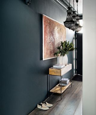 Narrow hallway ideas shown with dark gray walls, a slim console table and abstract wall art.