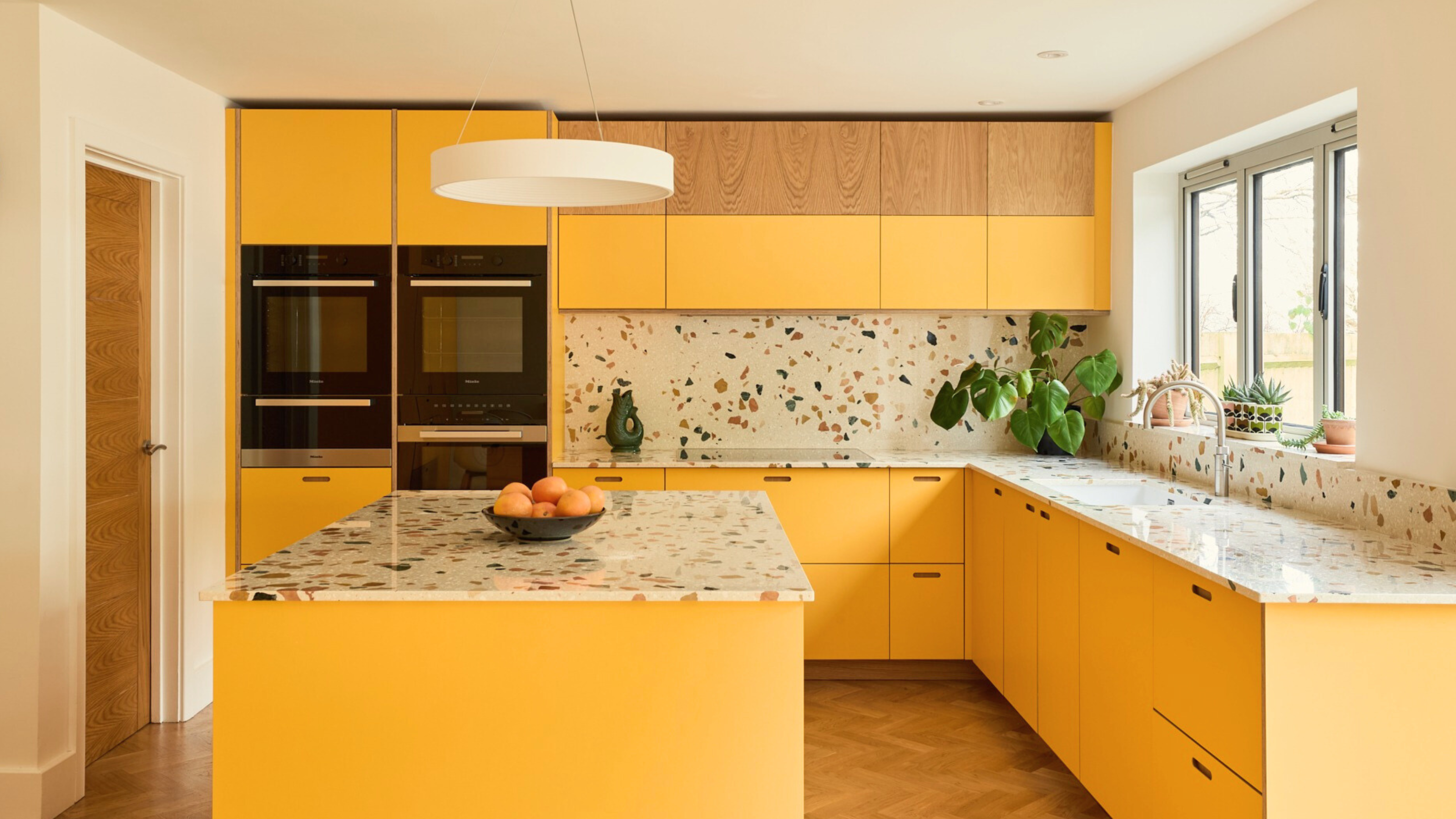 a large kitchen with yellow painted cabinetry and terrazzo countertops and backsplash