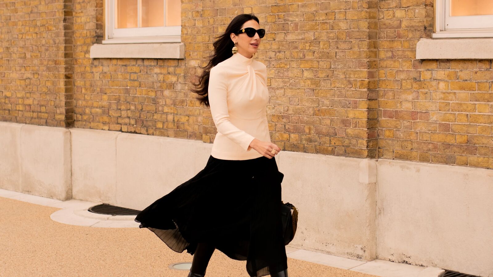 woman walks with long sleeve white top and long black skirt with tall boots 