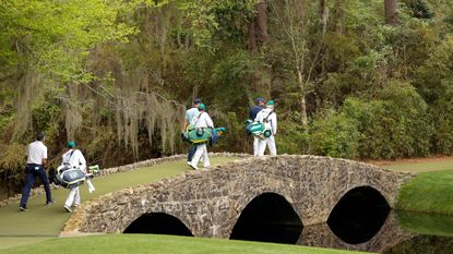 Golfers and their caddies cross the Nelson Bridge at Augusta National