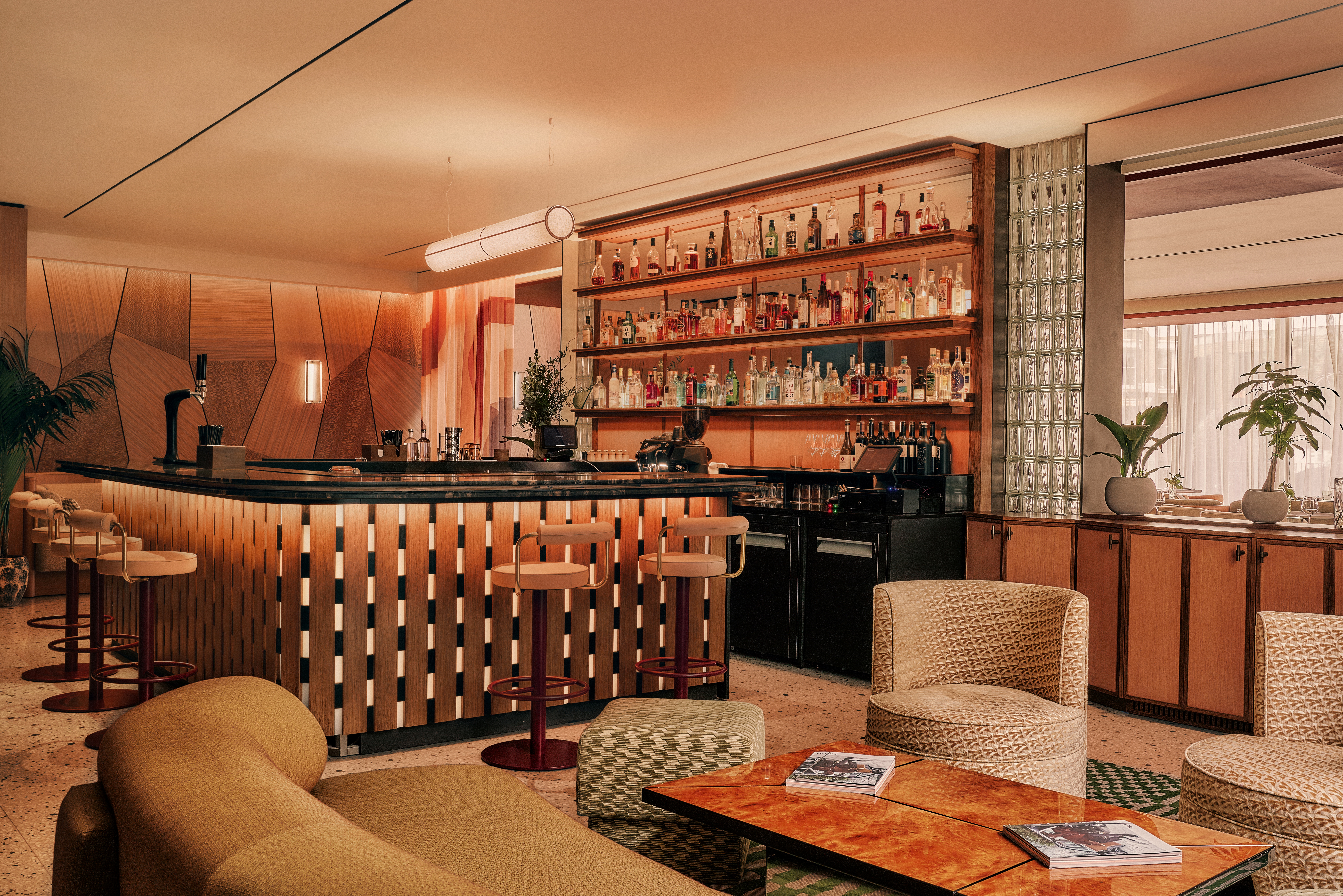 A hotel decorated with earthy hues, textural fabrics, sculptural wooden furniture with upholstered surfaces, thriving plants, abstract artworks, and warm lighting.