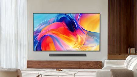 The Samsung M70H Mini-LED TV displaying colorful, abstract imagery from a wall-mounted position in a contemporary, well-lit living room