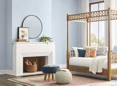 A living room with walls painted a light blue pastel shade with a fireplace and a four poster day bed