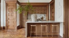 A wooden panelled kitchen with a marble top island in an otherwise whitye space