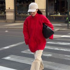 Influencer @annabelrosendahl crosses the street wearing a red jacket with cream trousers and brown trainers.