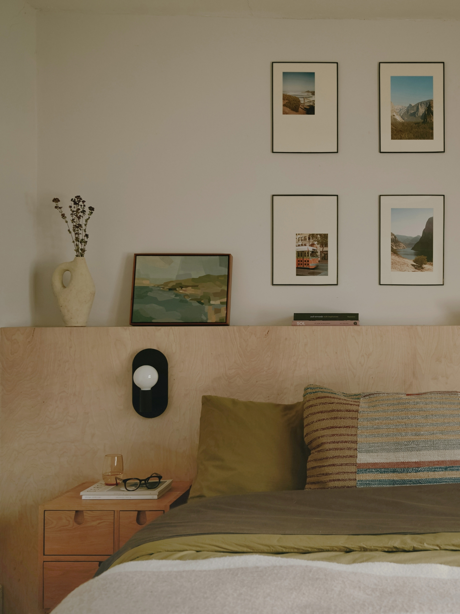 a bedroom with a plywood headboard and family photos on the wall behind, with green bedding on the bed