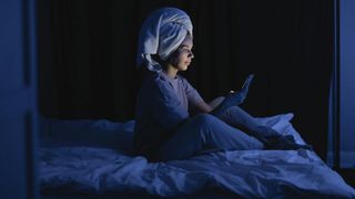 Woman sitting on bed at night using phone