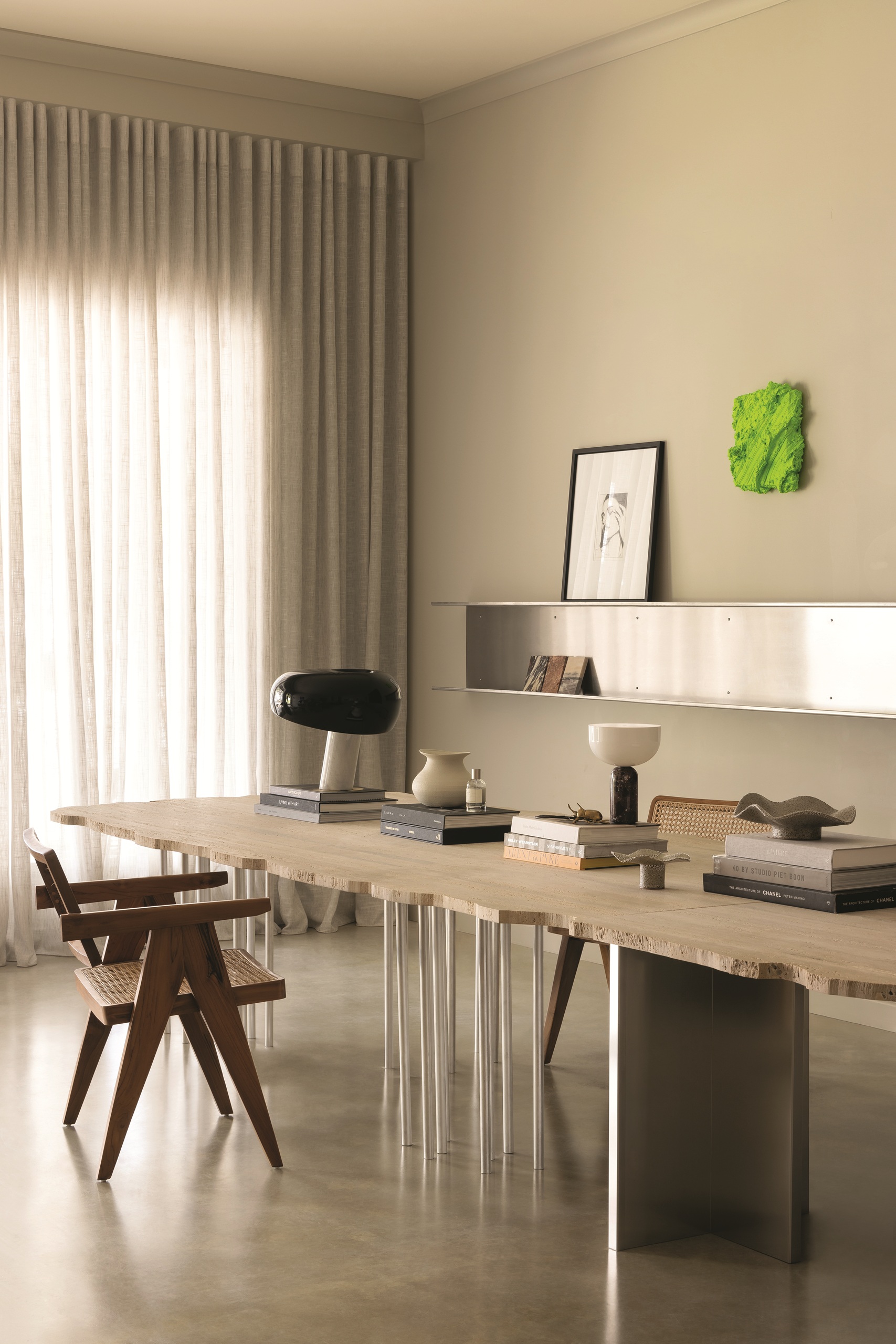 modern neutral room with sheer curtains, stainless steel shelving with art leaning and bright green artwork, travertine table with rough edge and stainless steel legs and armchair