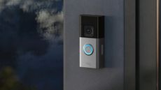 A Ring Battery Doorbell Pro mounted on a grey wall with a dark blurred background to the right