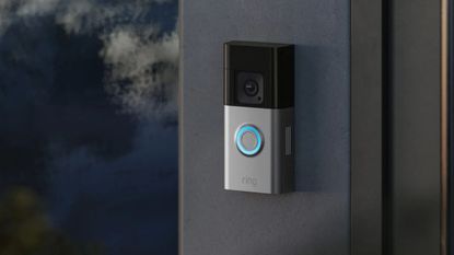 A Ring Battery Doorbell Pro mounted on a grey wall with a dark blurred background to the right