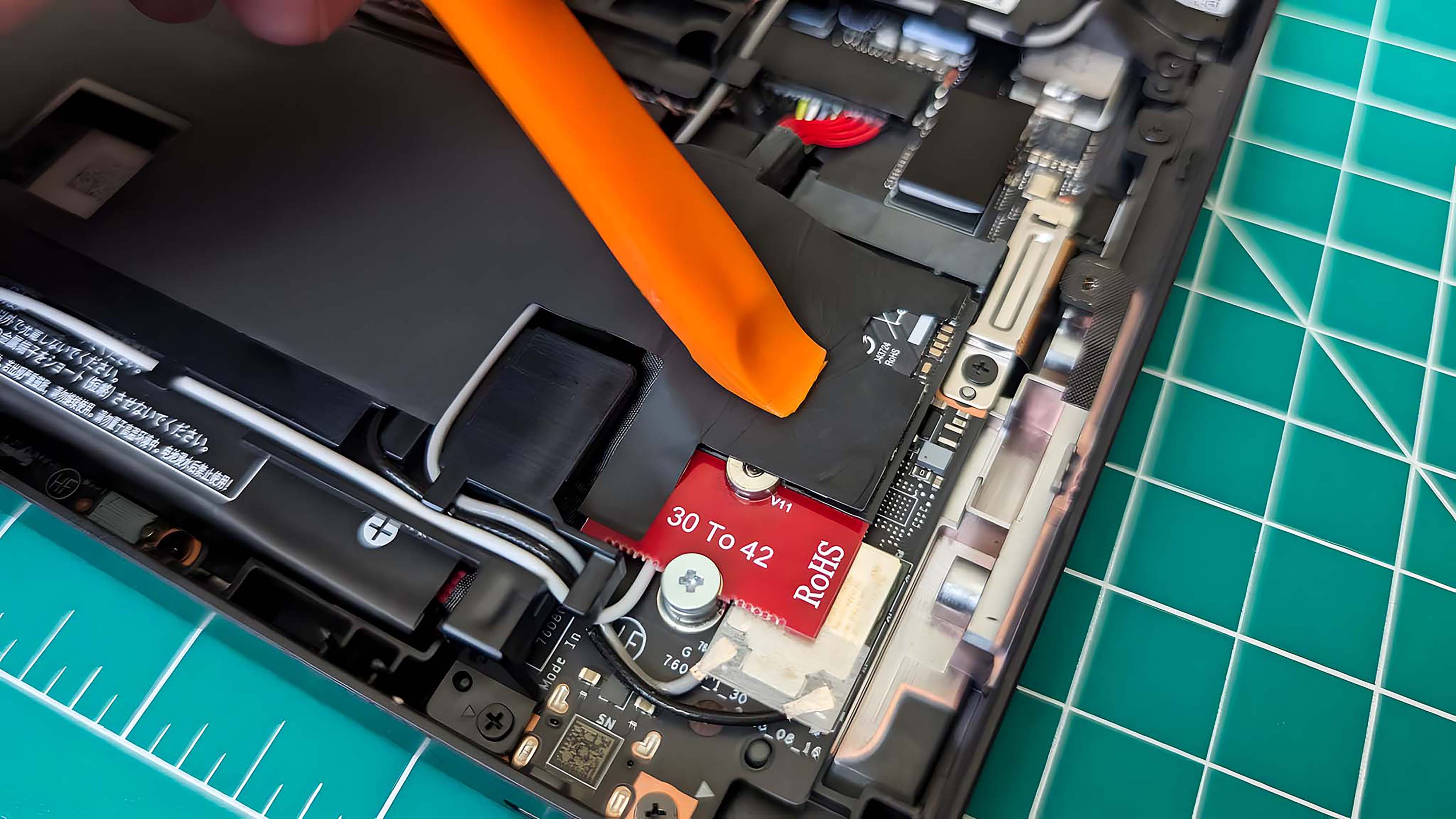 A prying tool being used to press the battery sticker back over the new SSD.