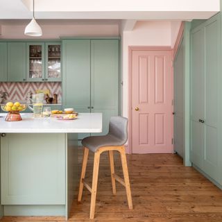 Kitchen with full height pale green units and a pink door