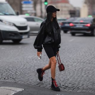 Yoyo Cao seen wearing black oversized leather jacket, black cycling shorts, black cap, red Loewe bag and black laced boots on March 04, 2022 in Paris, France.