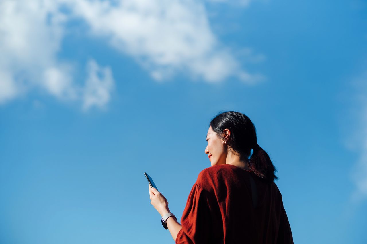 Woman looking at iPhone with blue sky in the background.