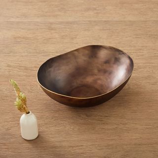 A brown bronze effect bowl with asymmetrical edges on a wooden surface