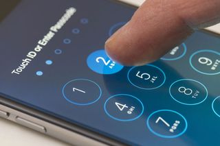 Finger typing passcode into iPhone screen.