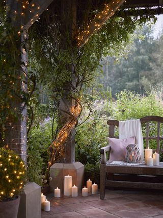 Outdoor fairy lights around tree trunks and LED candles in an outdoor seating area