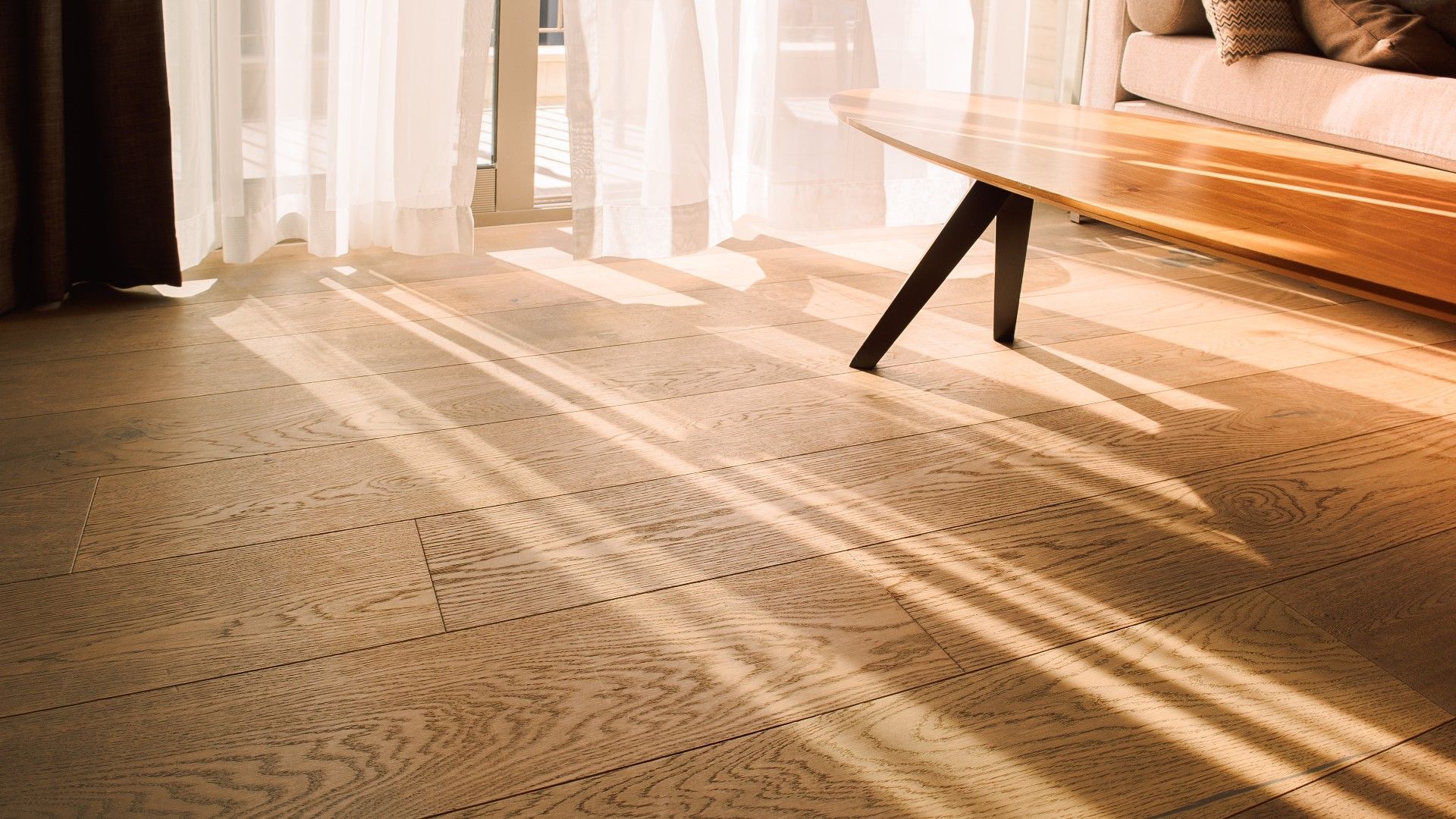 wooden floor with a coffee table and white curtains with sun streaming onto the floor