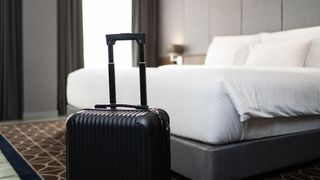 A black suitcase in front of a white bed in a grey hotel room