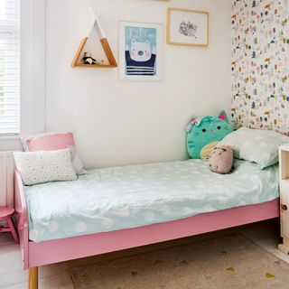 Childs bedroom with a pink bed wallpapered feature wall, blue polka dot bedding and cute cushions