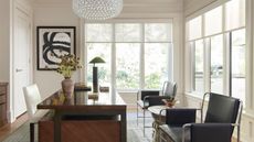 Home office with white walls, large windows, dark wood desk, midcentury leather metal chairs and abstract art