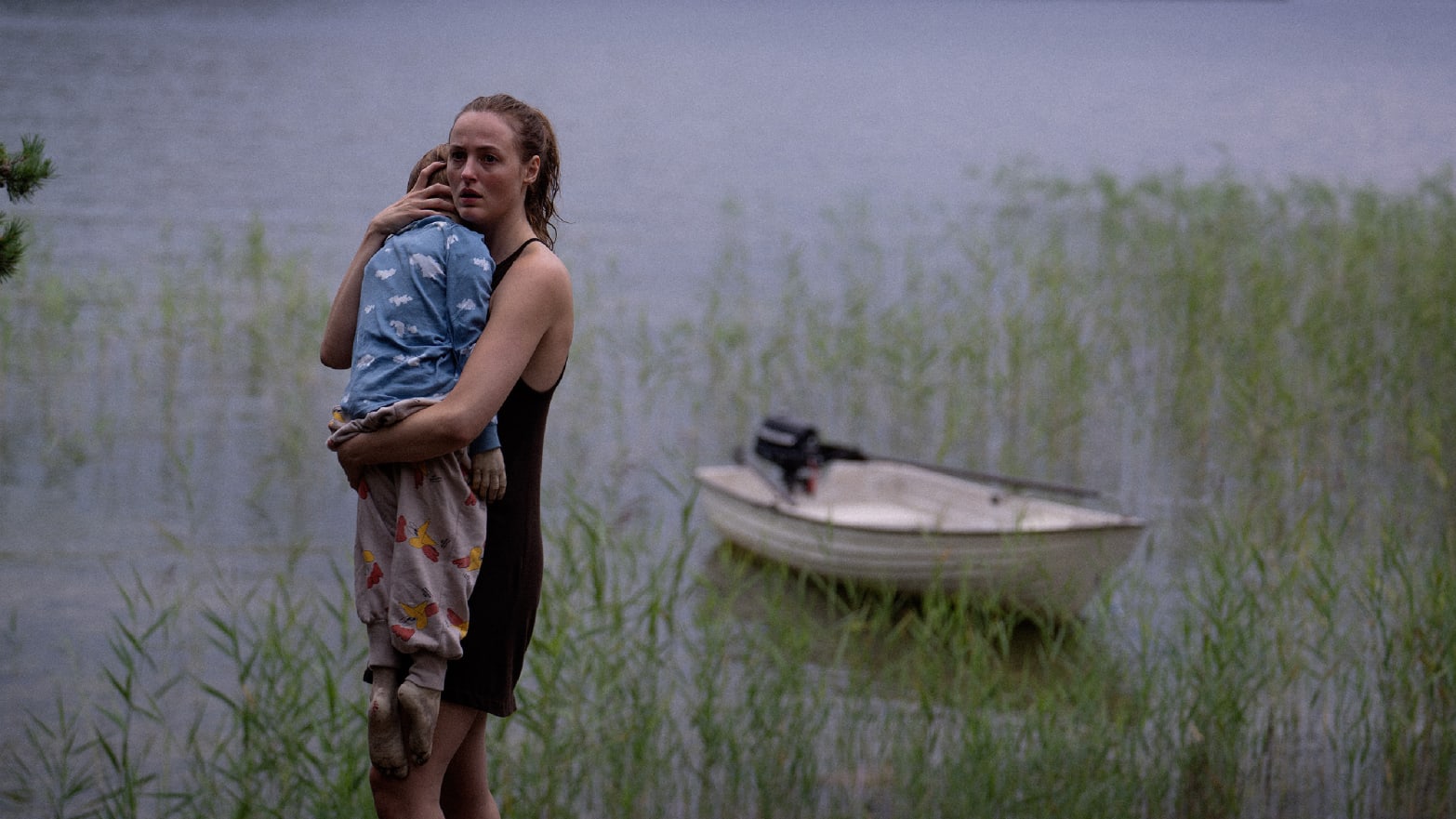 a woman holds a baby while standing in a marsh near a rowboat