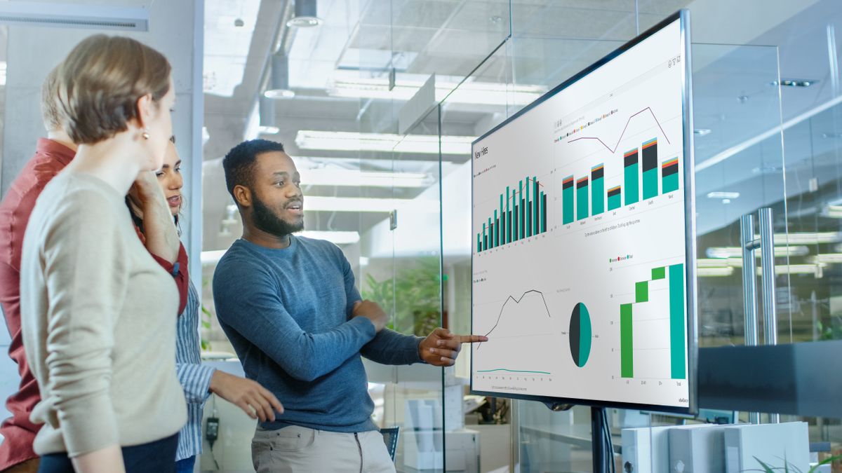 Two people presenting a Microsoft Excel spreadsheet on a large display. 