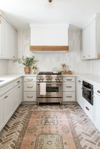 white small galley style kitchen with aged brick flooring and antique rug