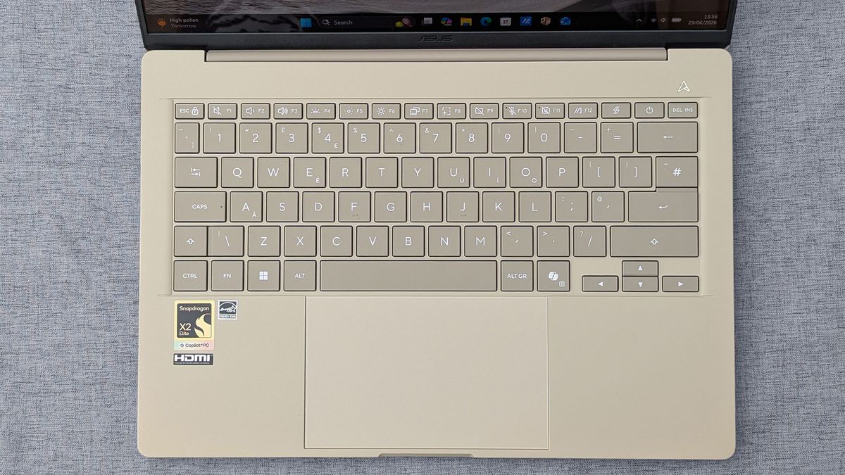 Top‑down view of a beige Zenbook A14 keyboard with Snapdragon X2 Elite and Copilot+ PC stickers, plus a centered touchpad.
