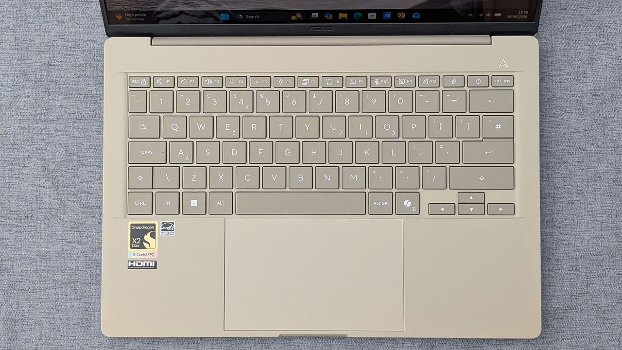Top‑down view of a beige Zenbook A14 keyboard with Snapdragon X2 Elite and Copilot+ PC stickers, plus a centered touchpad.