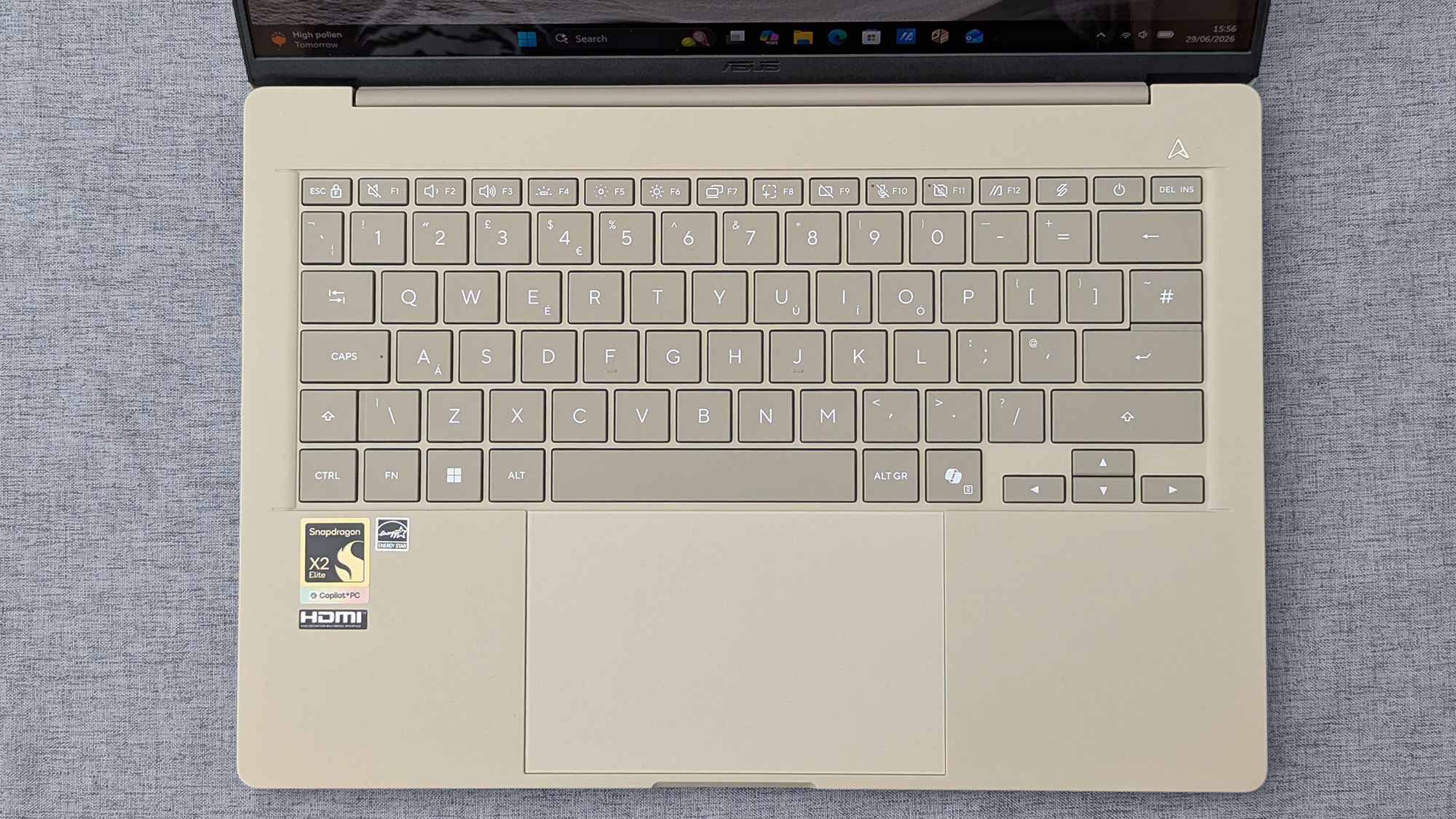 Top‑down view of a beige Zenbook A14 keyboard with Snapdragon X2 Elite and Copilot+ PC stickers, plus a centered touchpad.