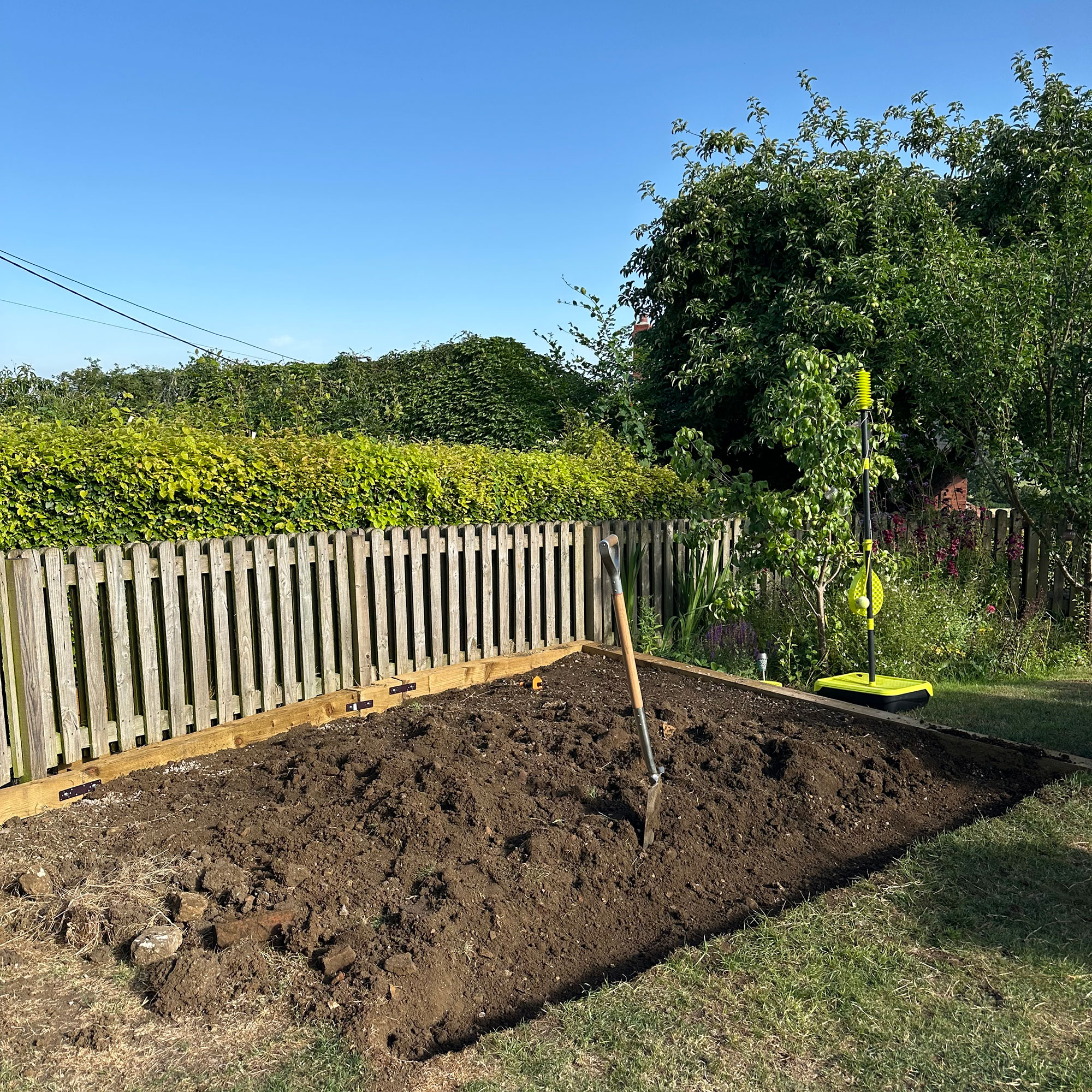 Flower bed beside wooden fence, dug up ready for planting