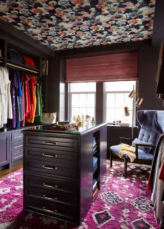 bright and colourful walk in wardrobe with open hanging, wallpaper on ceiling and pink rug