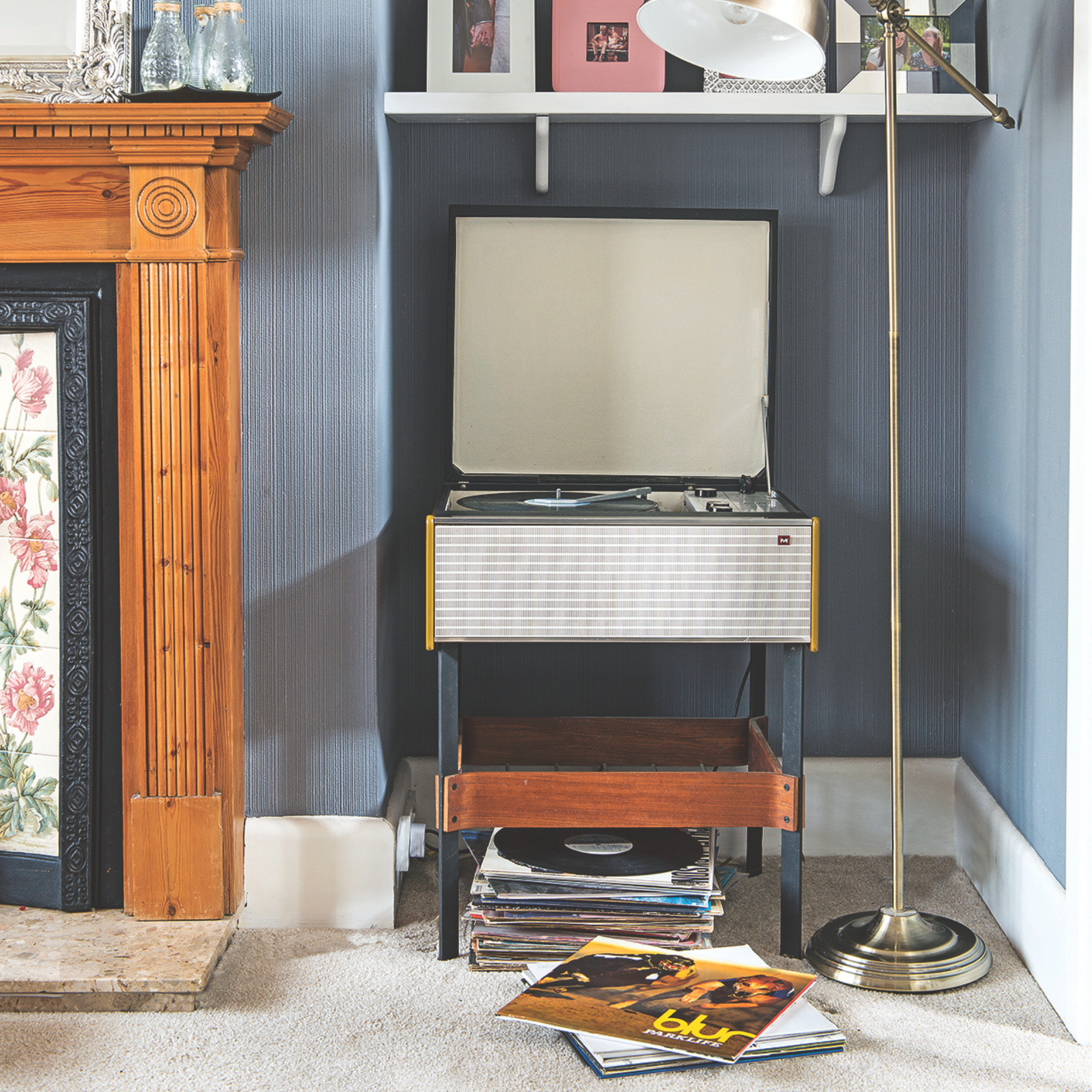 Living room detail with blue grey walls silver floor lamp and white wall shelves and vintage record player in alcove next to fireplace.