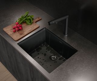 self cleaning black Bora kitchen sink with black tap inset into black worktop with wooden chopping board and red radishes