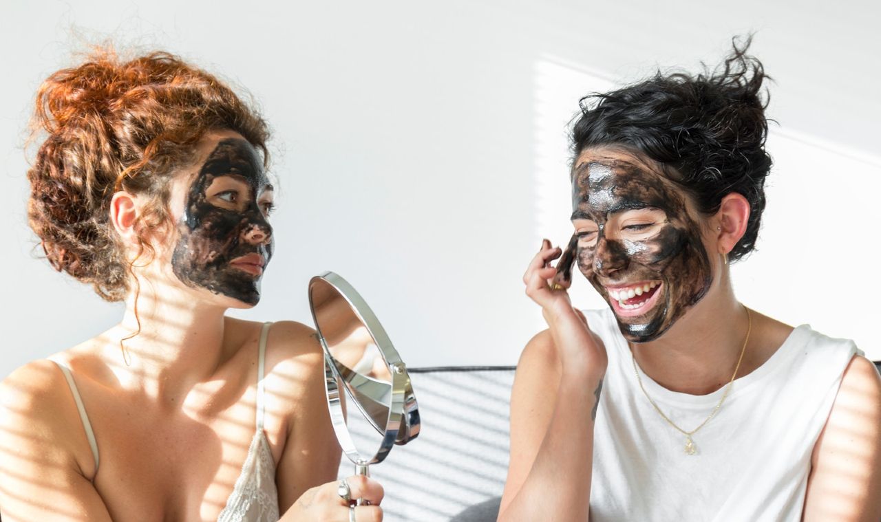 Two happy young women applying facial masks at home - stock photo