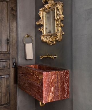 A moody powder room with a gold mirror and a pink natural stone sink