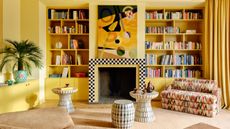 Bright yellow snug with built-in bookshelves either side of a fireplace with black and white checkerboard surround