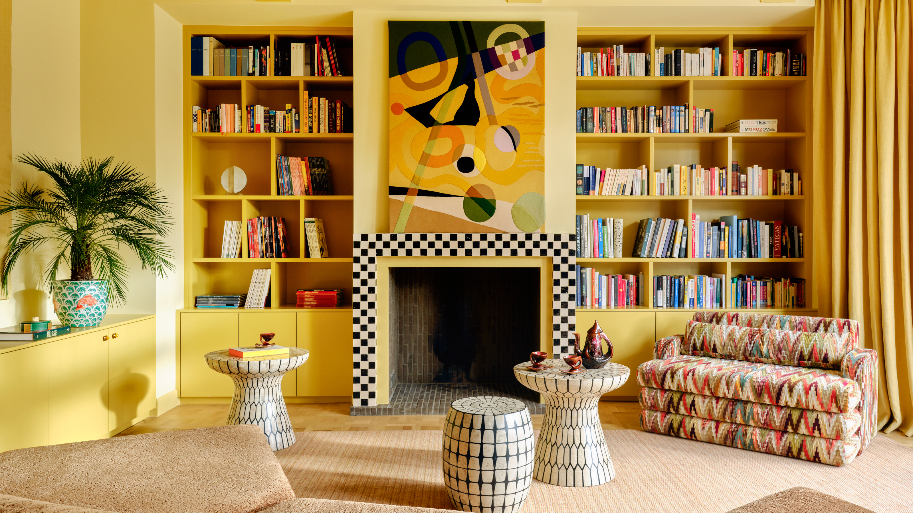 Bright yellow snug with built-in bookshelves either side of a fireplace with black and white checkerboard surround