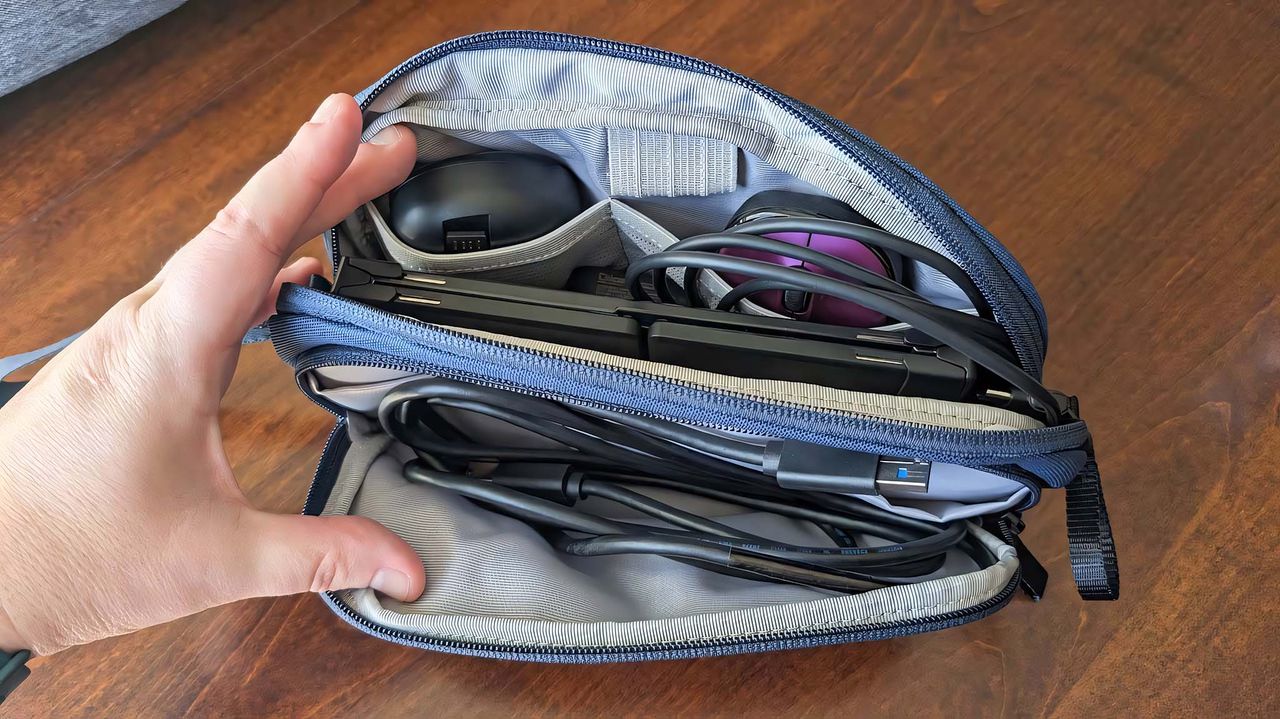 A blue Tomtoc Light-T12 Electronic Accessory Pouch M with zippers open and several accessories inside.