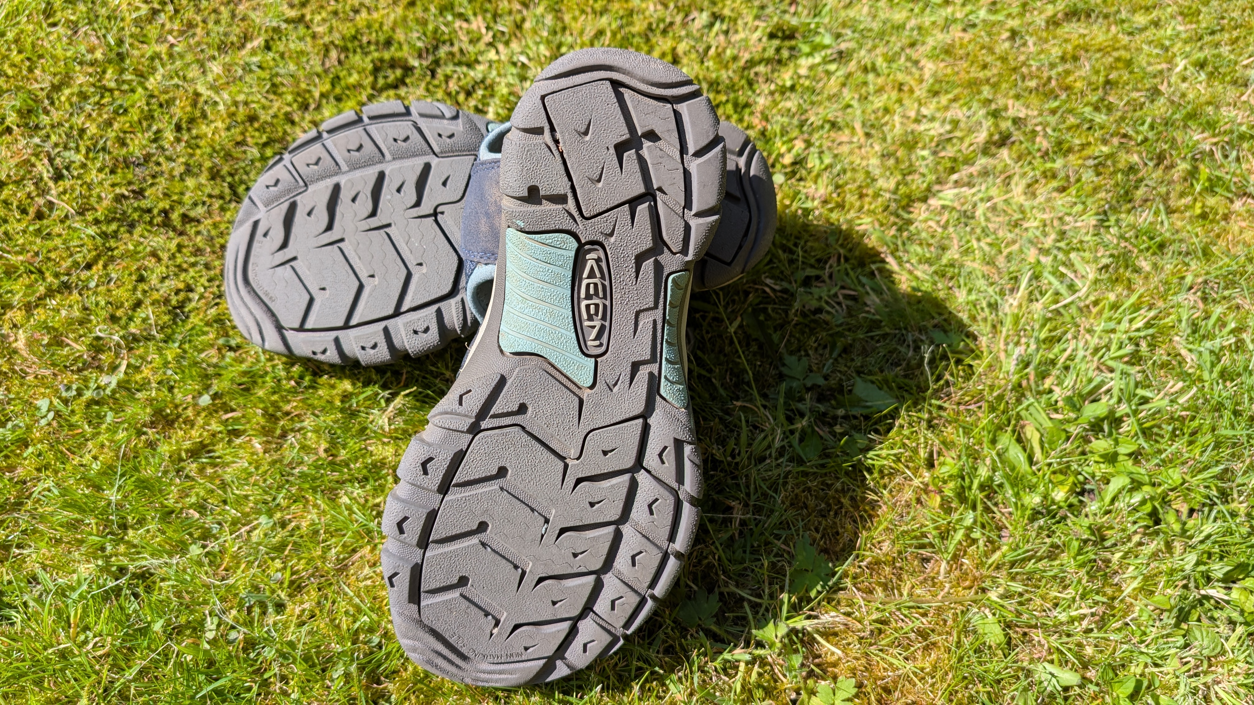 A pair of Keen Newport H2 hiking sandals lying on the grass with the soles facing up