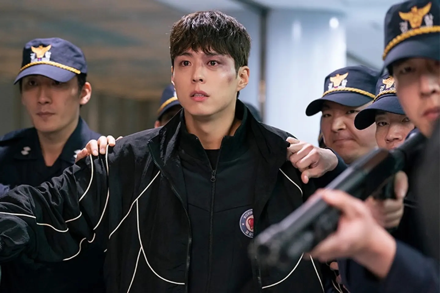 A man with a black eye (actor Park Bo-gum) stands amid a group of Korean police officers, in the K-drama 'Good Boy.'