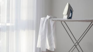 A steam iron sitting on an ironing board with a white shirt draped over the end