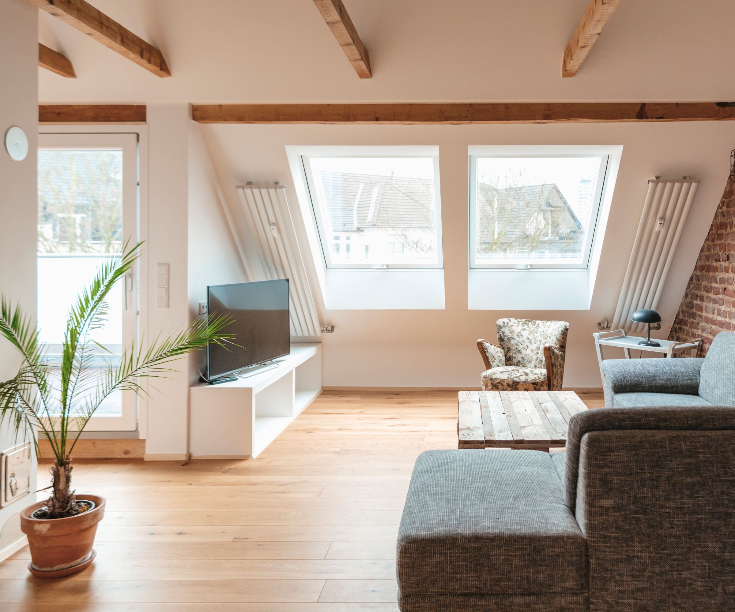A living room with a grey sofa and wood flooring in a loft conversion with rooflights and a separate sliding glazed door out to a balcony