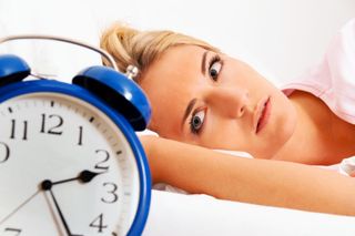 A woman lays in bed, unable to fall asleep, looking at a clock.
