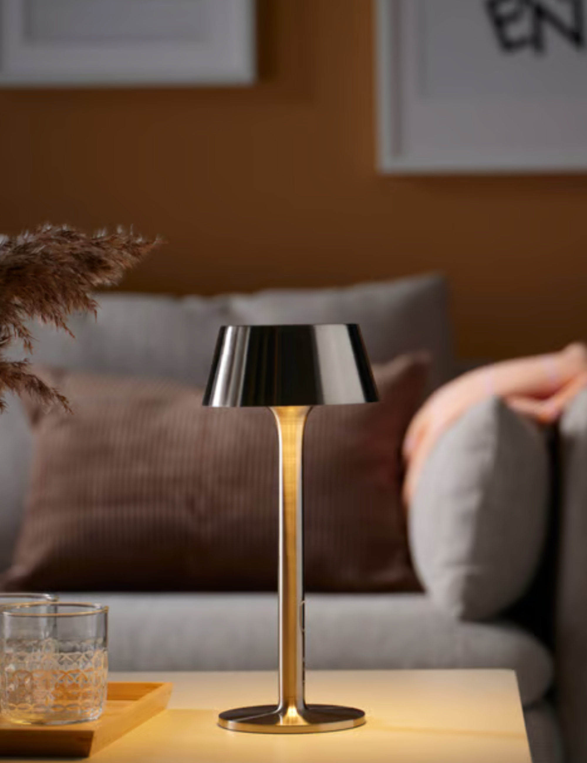 Chrome IKEA portable indoor / outdoor lamp styled atop of a wooden coffee table alongside a tray of crystal-cut glasses