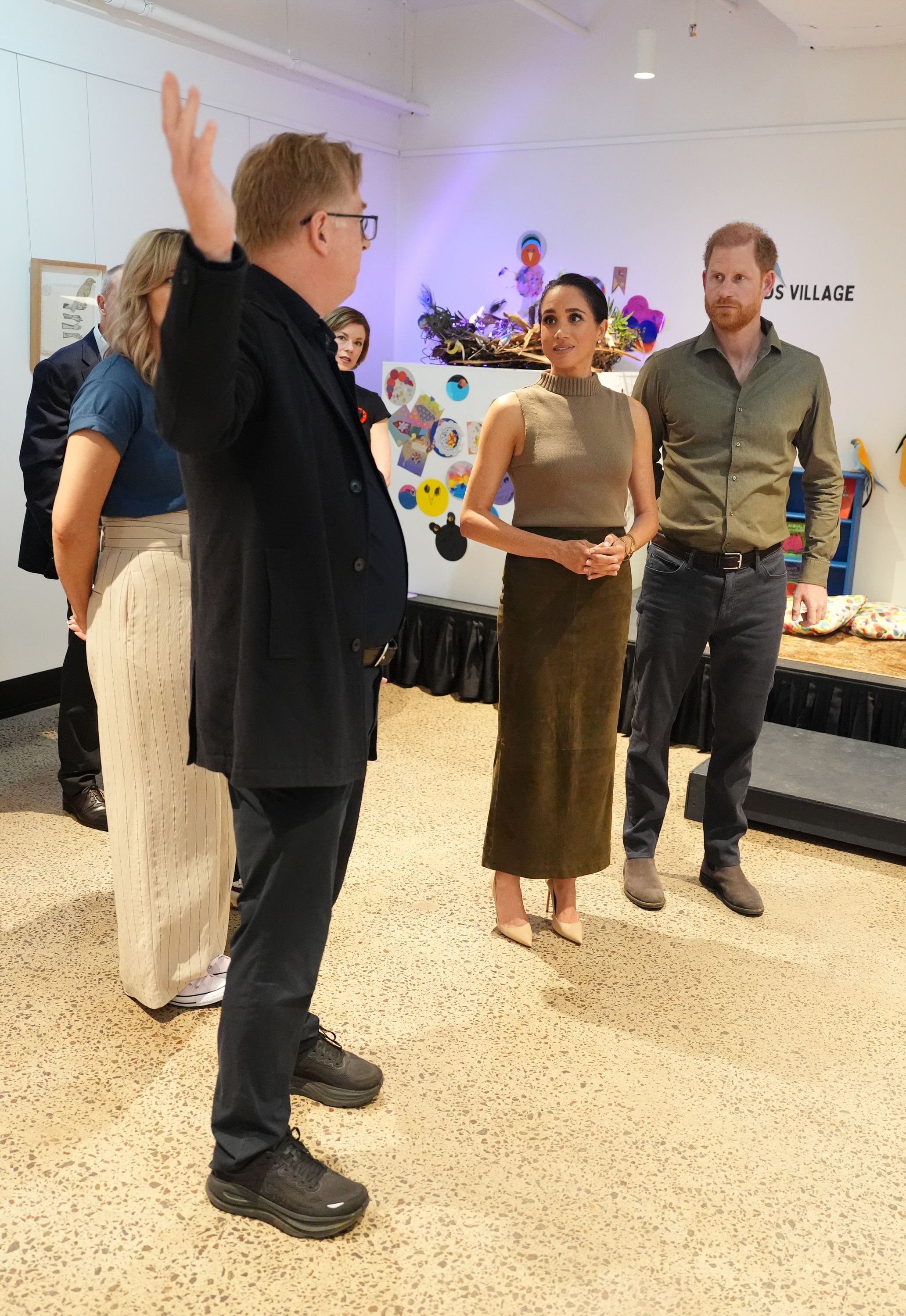 Meghan Markle wearing a green skirt and sleeveless top talking to people at a museum