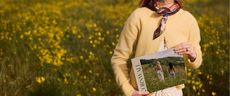 Model holding a personalised photobook sold at Papier stood in a field of wild flowers