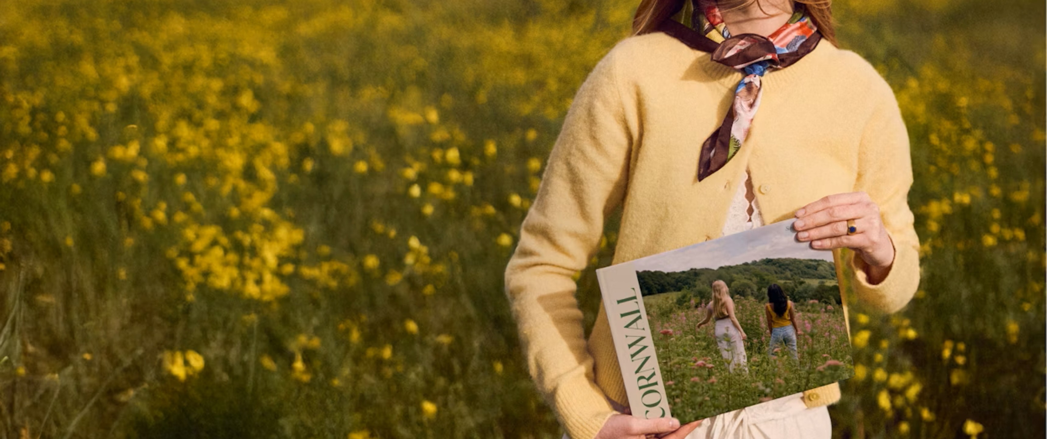 Model holding a personalised photobook sold at Papier stood in a field of wild flowers 