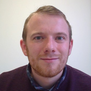 male with short light hair, trimmed beard wearing blue shirt with burgundy jumper